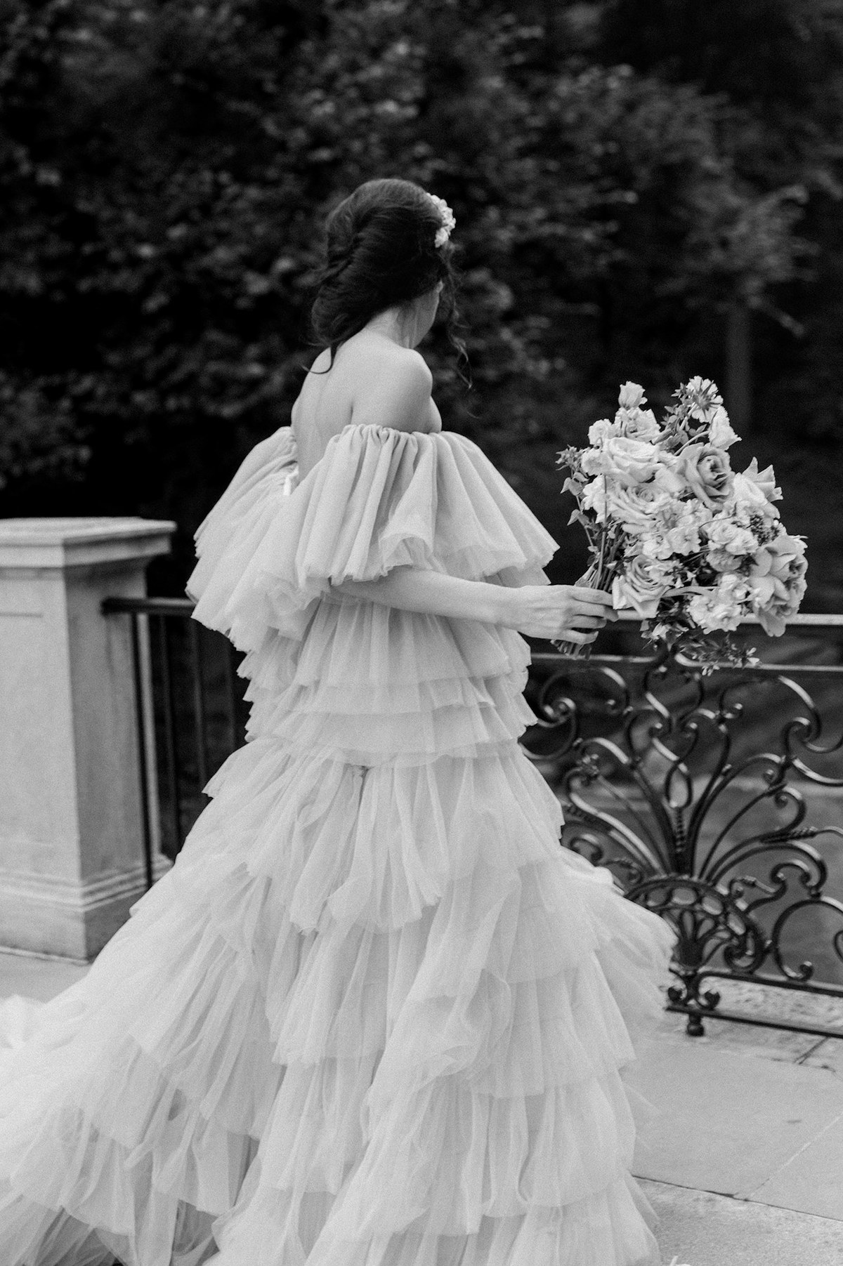 Bride, adorned in a tiered couture gown in soft mauve, radiates timeless beauty in a stunning black and white portrait at Longwood Gardens.